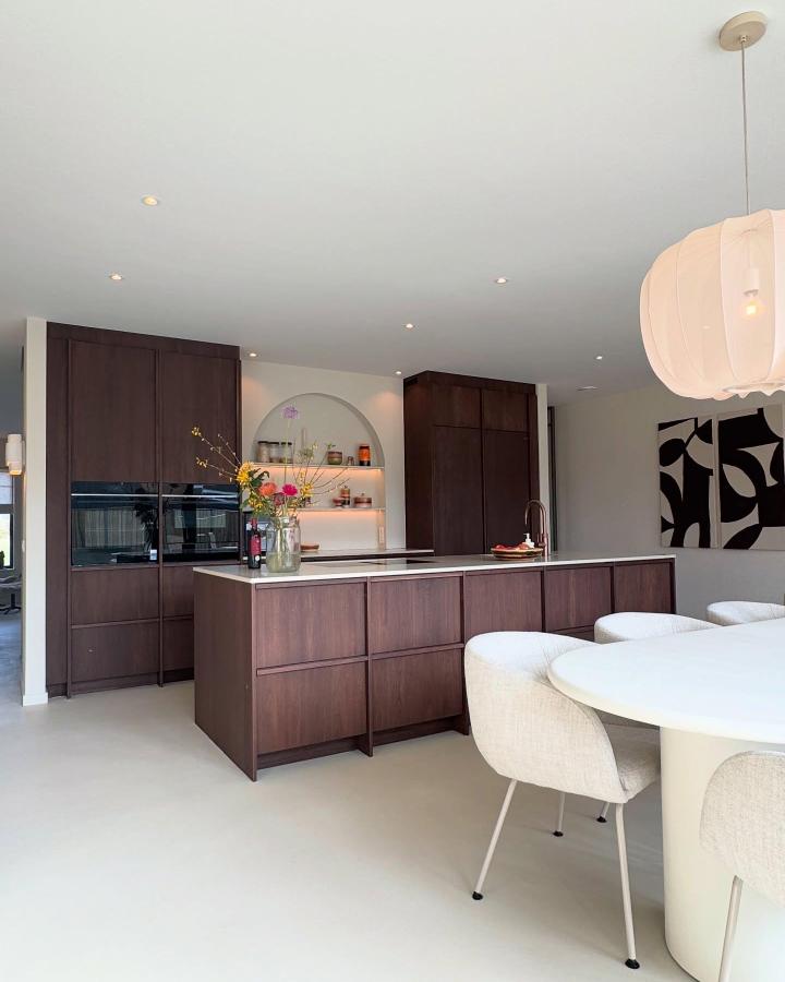 Dark wood kitchen island from @deontwerpboer featuring handleless drawers and pale flooring contrast.