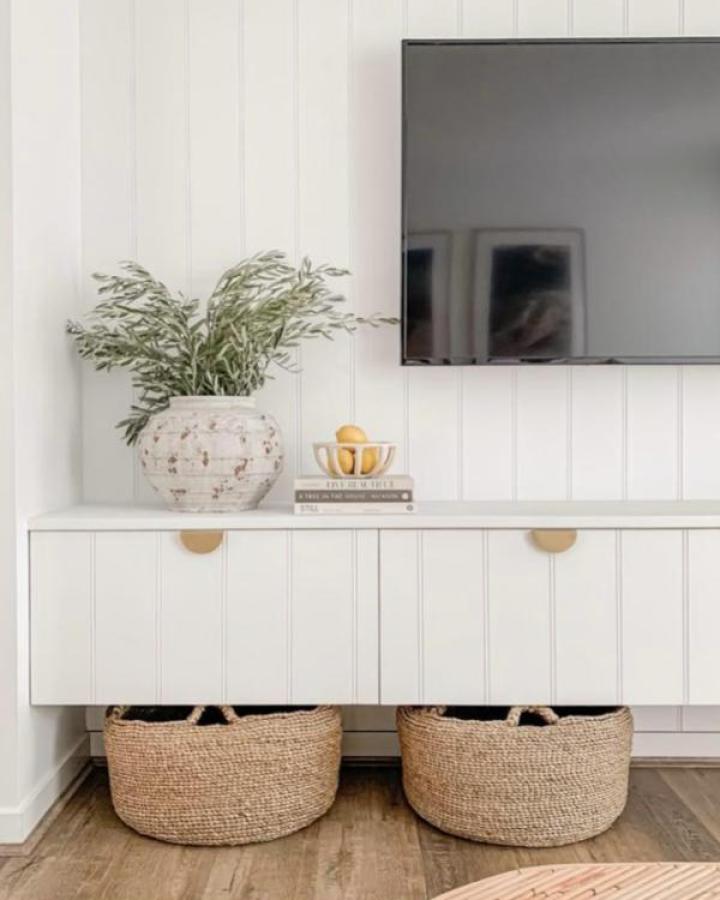 White paneled media cabinet from The Interiors Addict with brass pulls and woven storage baskets below.