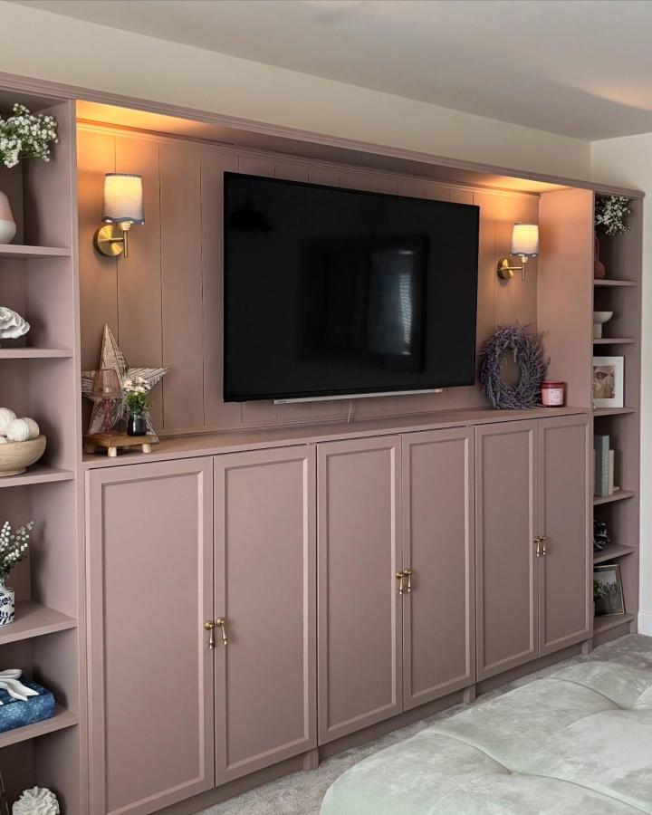 Dusty rose built-in media unit from @lifewithbecx with brass sconces and open shelving.