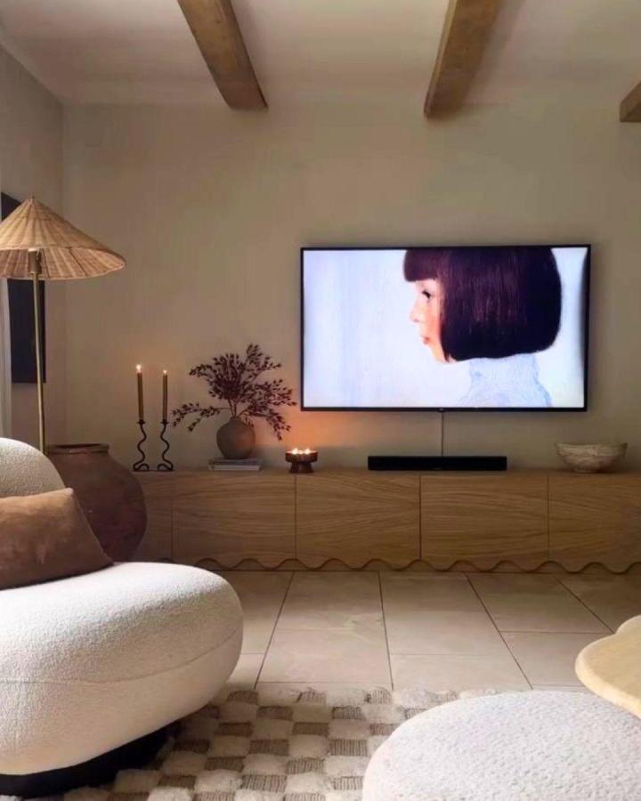 Scalloped oak media console from @mishkashoe with warm candlelight and textured seating below mounted screen.