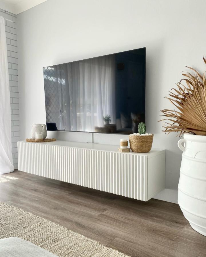 White fluted IKEA Besta media console from @the_coastalflat with wall-mounted TV and coastal decor accents.