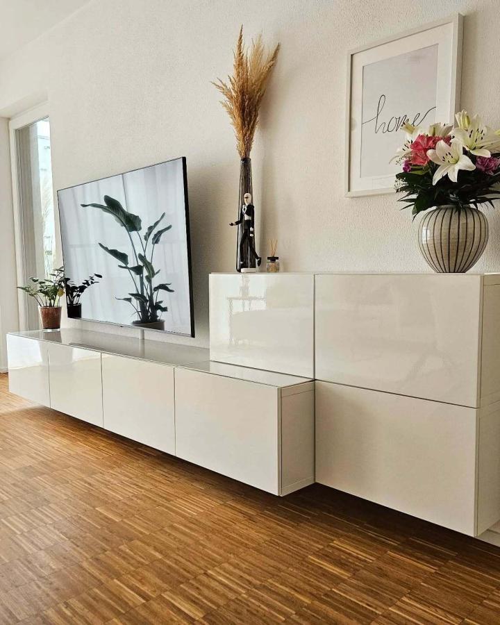 Glossy white floating media console from @diy_home_living with botanical artwork and fresh flowers above.