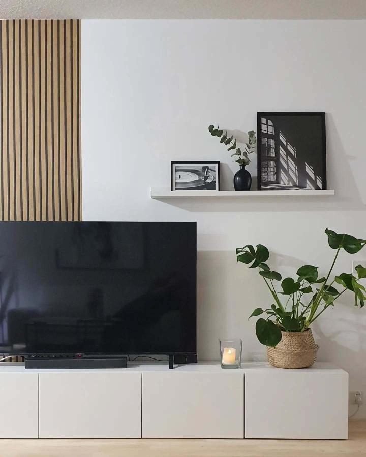 White media console from @marita.villejalupiineja. Floating shelf with monochrome art and natural greenery accents.