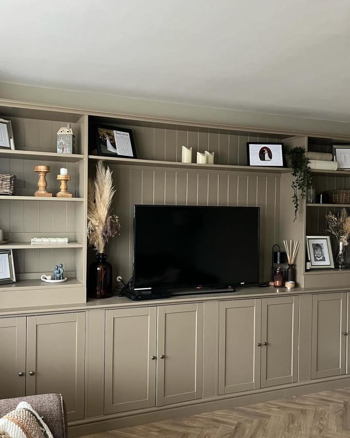 Sage green paneled media wall from @turner_no13_home with built-in shelving and copper decor accents.