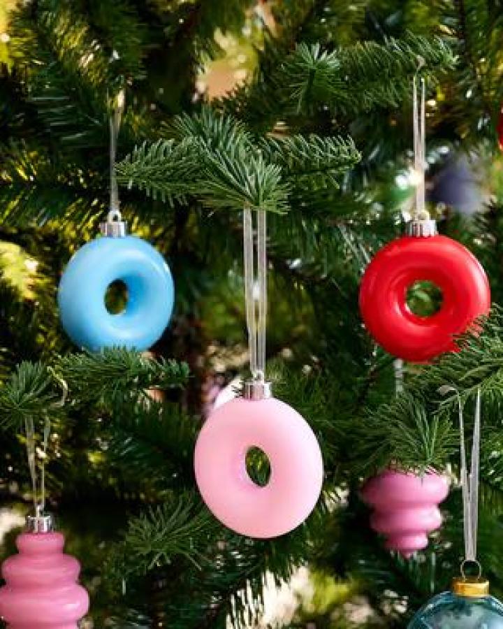 Glossy donut-shaped ornaments from Ikea. Pink, blue, and red baubles hanging on evergreen branches.
