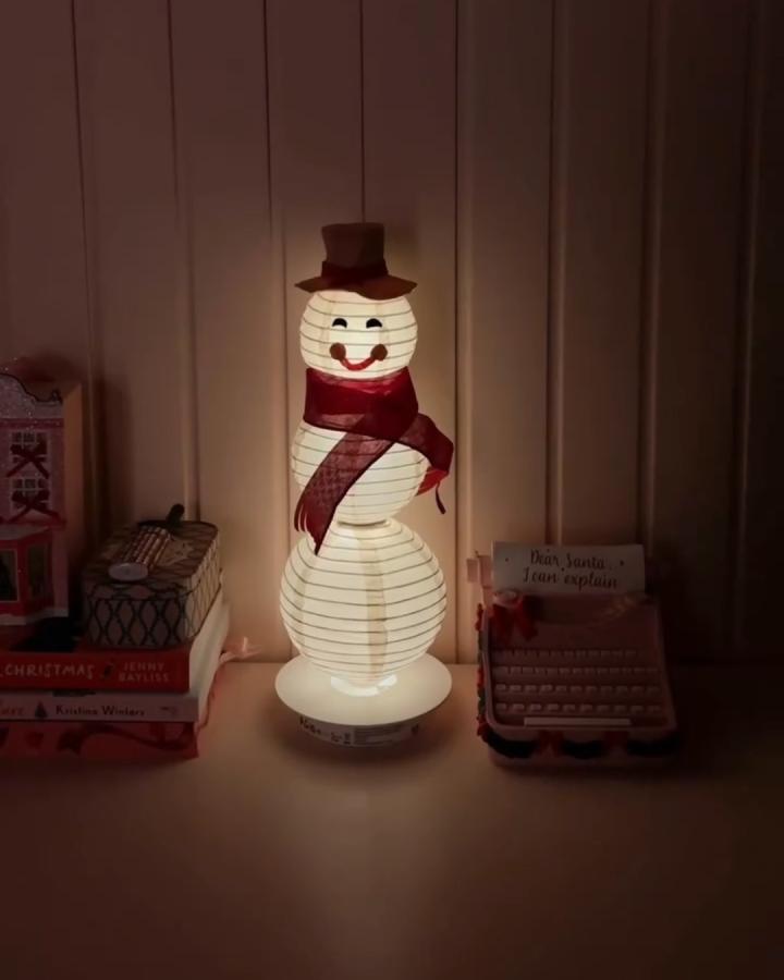 White paper lantern snowman craft from @fleurmaison with burgundy hat and scarf glowing warmly.