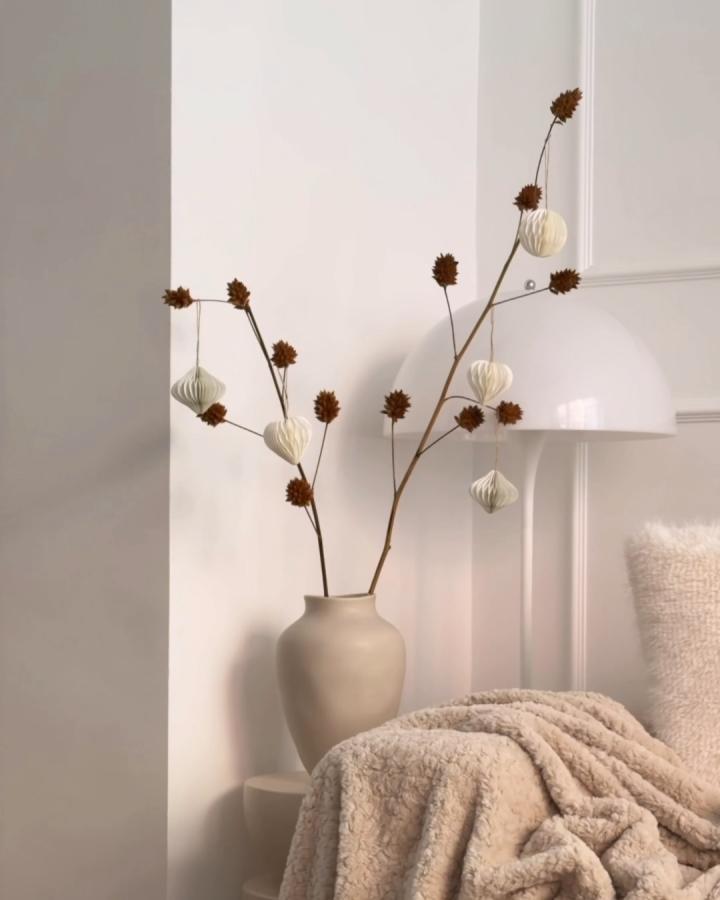 Cream pleated paper ornaments on dried branches from @howimetmyoutfit. Minimalist holiday vase arrangement with natural elements.