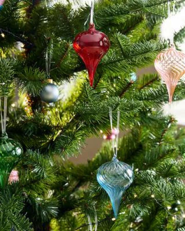 Elongated glass baubles in crimson, blue, and champagne tones from Ikea. Vintage Christmas ornaments on green tree.