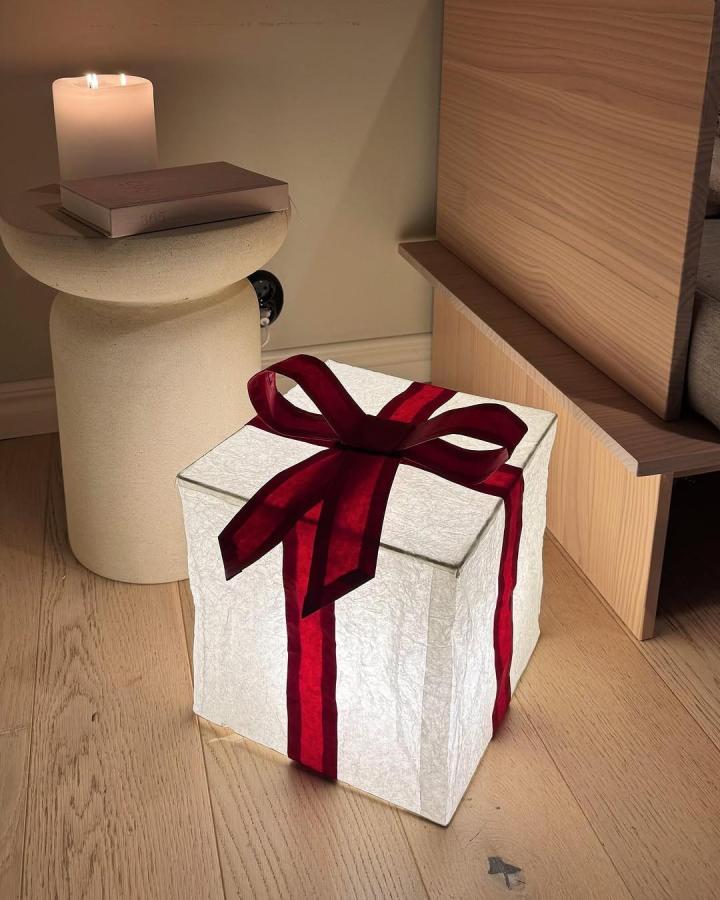 White textured gift box lamp from @yayanaomi with deep red ribbon beside candle and wood shelving