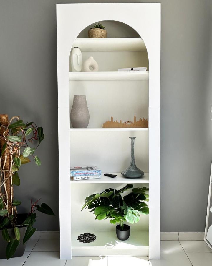 White arched bookcase from @guippdecor featuring ikea anthropologie hacks & ideas with plants and ceramics displayed.