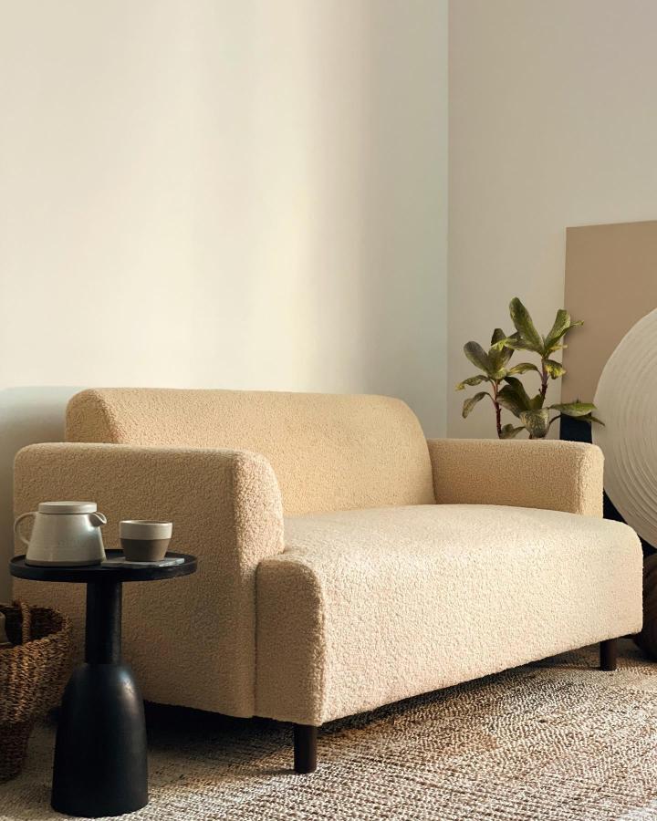 Creamy boucle upholstered sofa from @dalia.ea. Paired with black sculptural side table and jute rug.