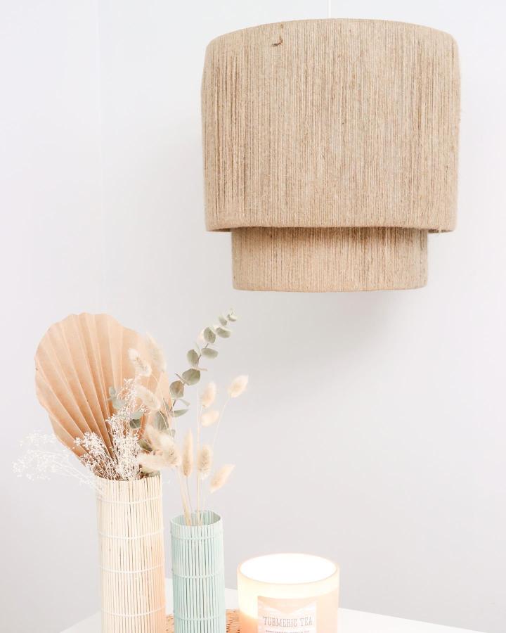 Natural jute tiered pendant light from @katiebookser with dried floral arrangement and candle below.