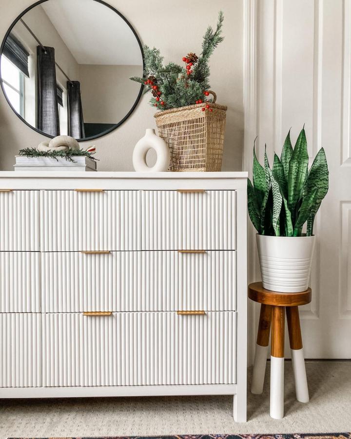 White fluted dresser from xomyhome featuring textured drawer fronts and brass hardware with mirror and greenery.