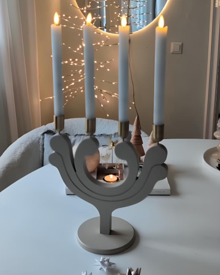 Grey sculptural candle holder from @herzenstimme with pale blue tapers and twinkling lights behind.