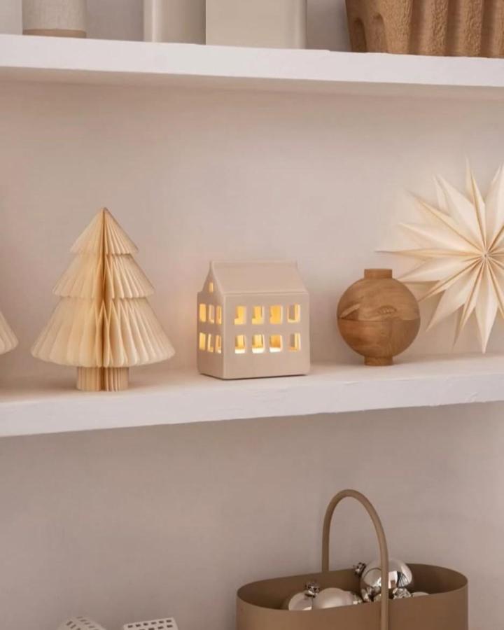 Cream paper tree and ceramic house on white shelf from @howimetmyoutfit. Neutral holiday styling.