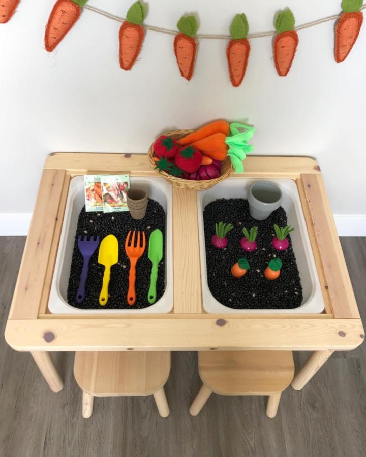 Natural wood sensory table from @lifewith.z. Black beans fill bins with felt vegetables and colorful tools.
