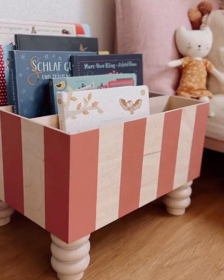 Coral striped Moppe chest from @kruthdesign with wooden ball feet holding children's books and toys.