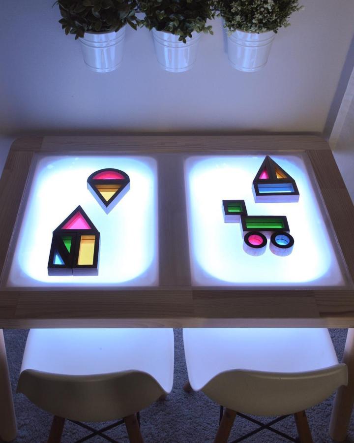 Natural wood light table from @unknitandtiedtogether with colorful geometric blocks and hanging plant decor.