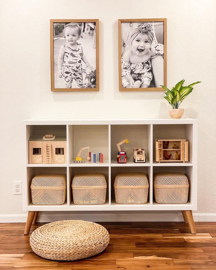 White cube storage unit from @brittanyhuffmon with rattan baskets and wooden mid-century legs displaying toys.