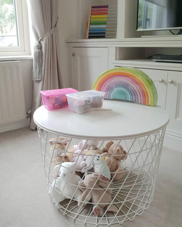White wire basket table from @for.the.love.of.greige with stuffed toys inside and rainbow stacker on top.