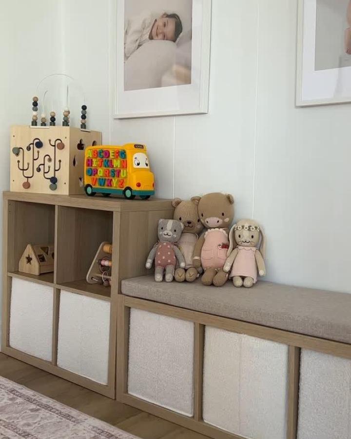 Natural wood Kallax storage bench from @stylewithgigi showing ikea playroom storage hacks & ideas with gray cushion and cream bins.