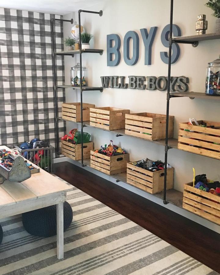 Industrial pipe shelving with wooden toy crates from @mbhomedesigners. Boys playroom with metal wall letters.