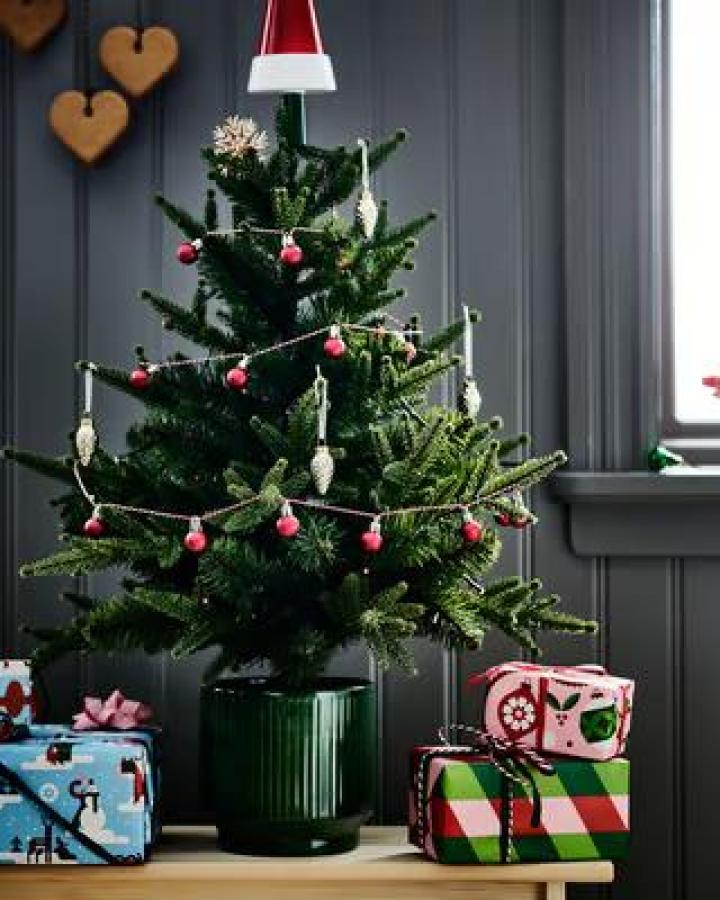 Green Christmas tree from Ikea decorated with pink baubles and cream garland against dark paneled wall.