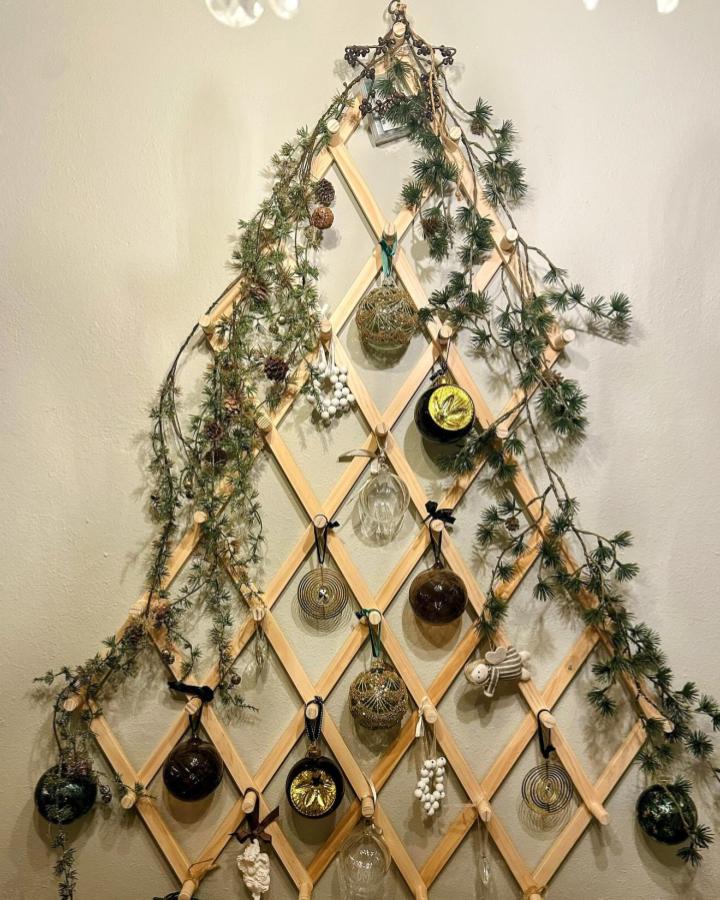 Natural wood trellis display from @marys_skap_gode_minner_ with ornaments and pine garland in diamond pattern.