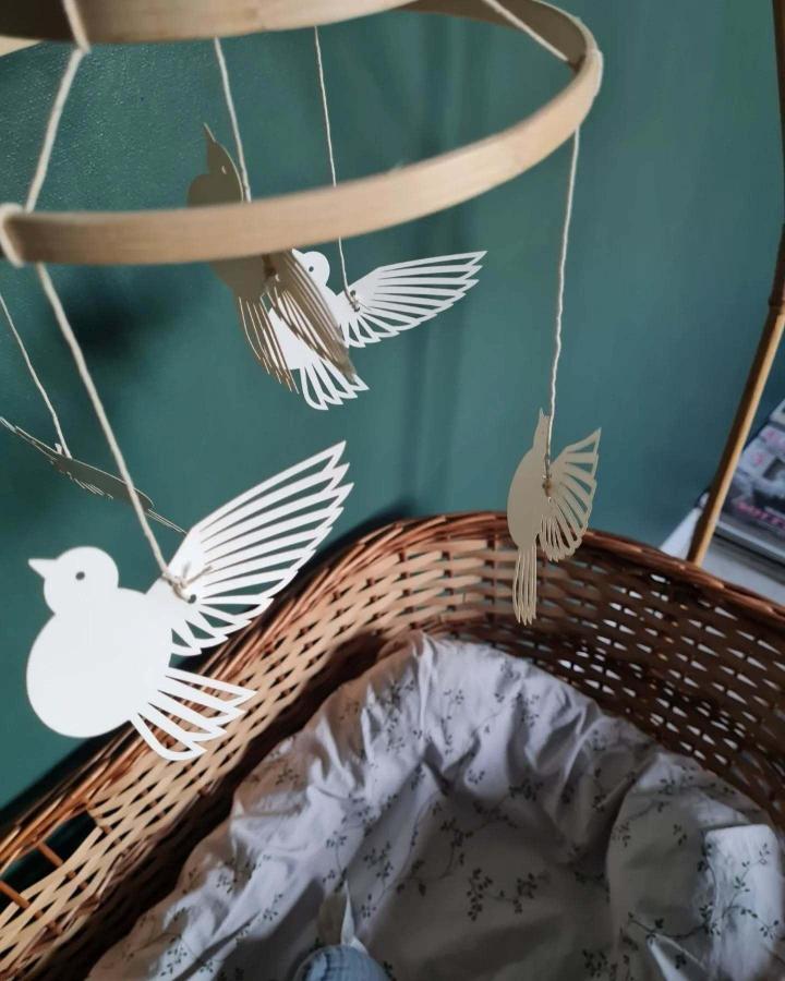 White paper bird mobile from @eneledamm hanging above woven bassinet with botanical bedding