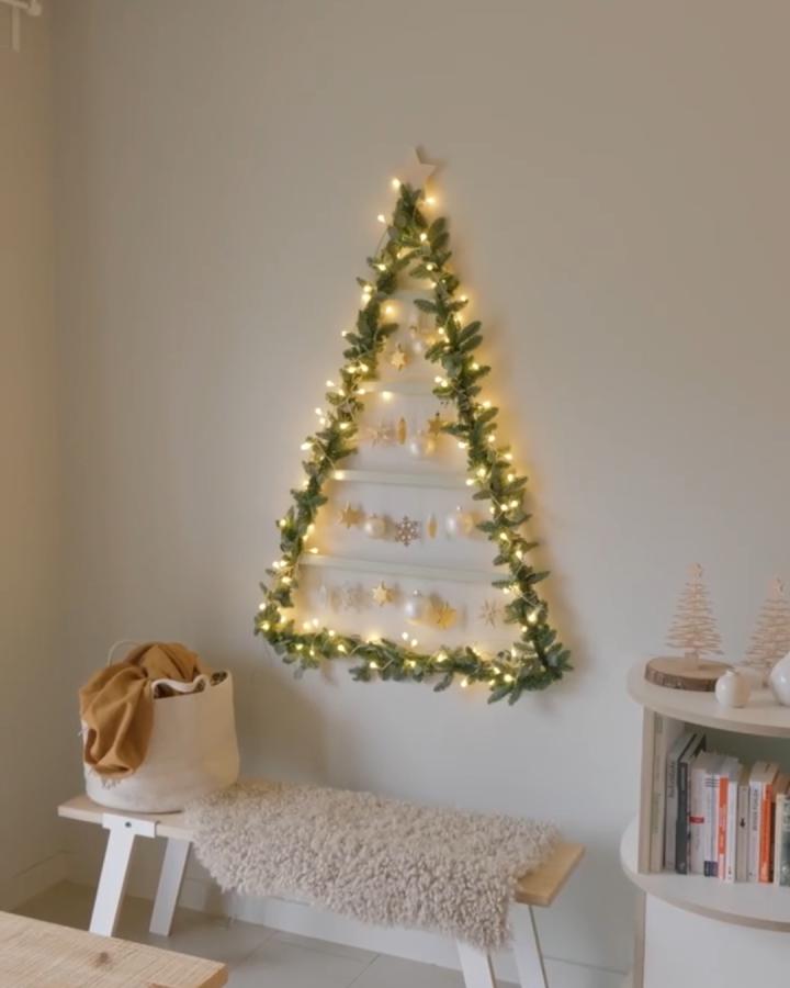 Wall-mounted triangle tree from schere leim papier with garland, lights, and ornament shelves.
