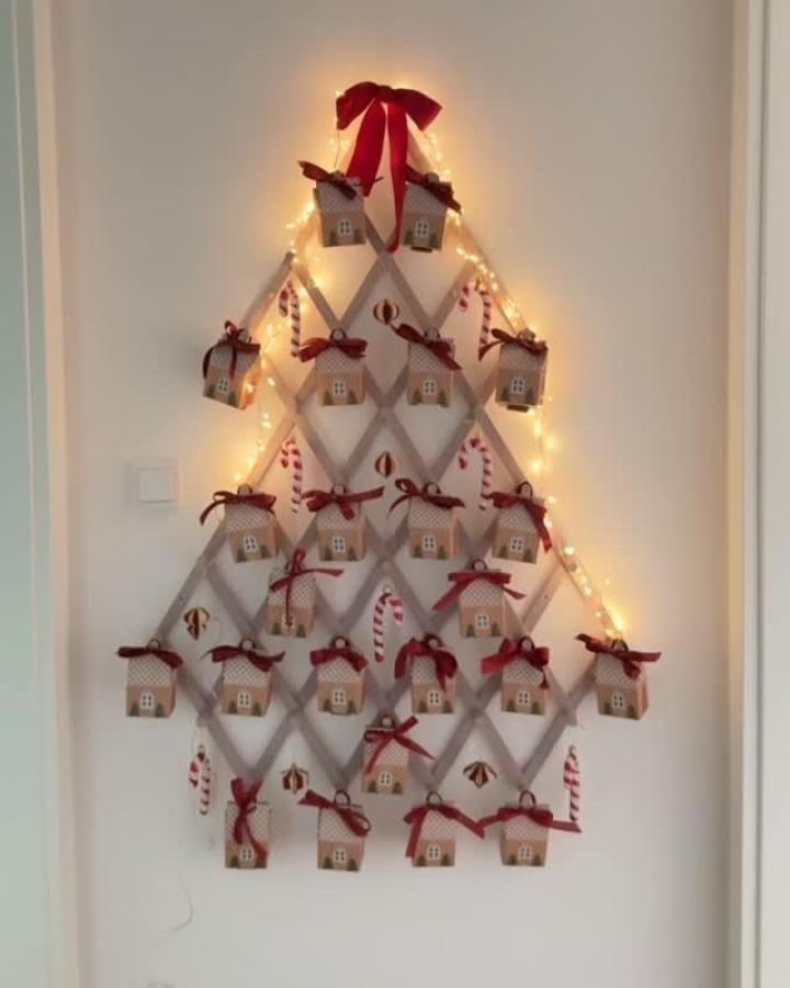 Beige fabric advent calendar wall display from @interior.with.sabi. Gingerbread houses with red bows and string lights.