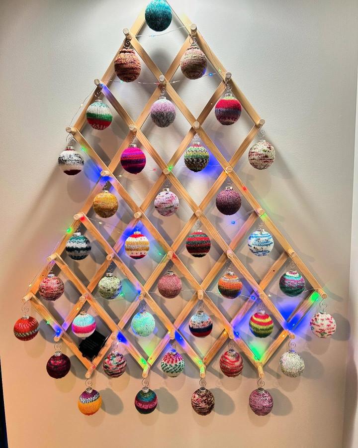 Wooden lattice display filled with colorful knitted ornaments from @akaroxy. Festive wall-leaning holiday arrangement.