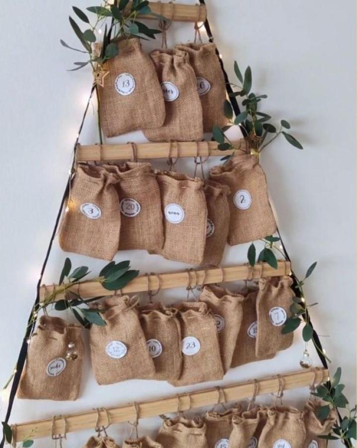 Natural burlap advent calendar from @my_nordic_home_am_see with numbered bags on bamboo ladder frame and olive branches.
