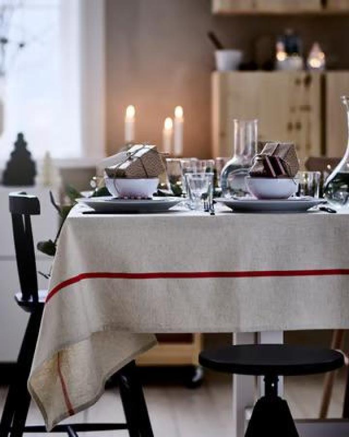 Off-white linen tablecloth with red stripe from Ikea. Candles and wrapped gifts create festive dining setup.