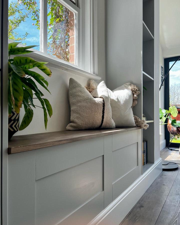 Sage-green paneled window bench from @home.at.highfield with textured pillows and wood seat.