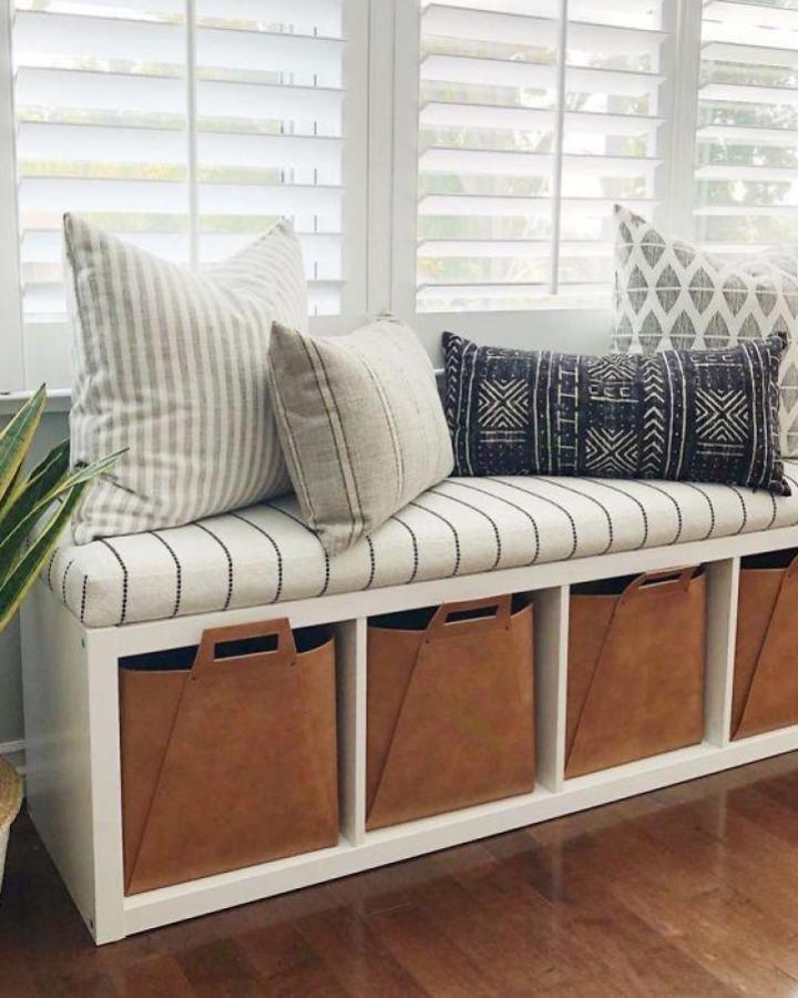 White Kallax window bench from @theheartandhaven with striped cushion and tan storage bins below shutters.