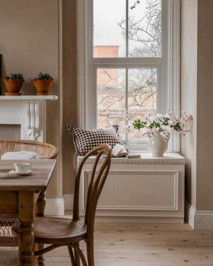 Cream panel-molded window bench from @nicolahuthwaite. Gingham cushion and pink blossoms complete the look.