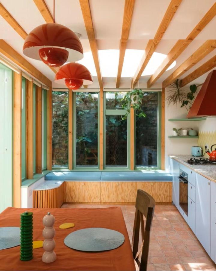 Pale blue cushioned L-shaped bench with plywood paneling from Plykea in a bright kitchen corner.