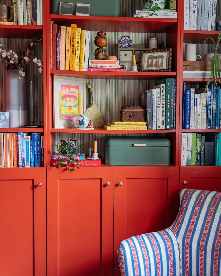 vibrant coral Billy bookcase with cabinet doors and colorful books from @rosieandthefarm in a cozy reading corner