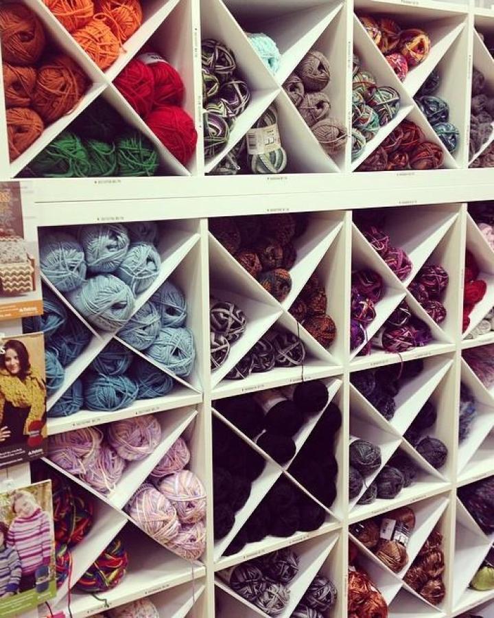 White shelving unit with X-shaped dividers filled with colorful yarn skeins showcasing ikea craft room storage hacks from @allaboutami.
