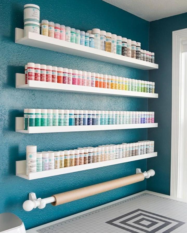 white floating shelves with colorful paint bottles on teal wall ikea craft room storage hacks with paper roll below