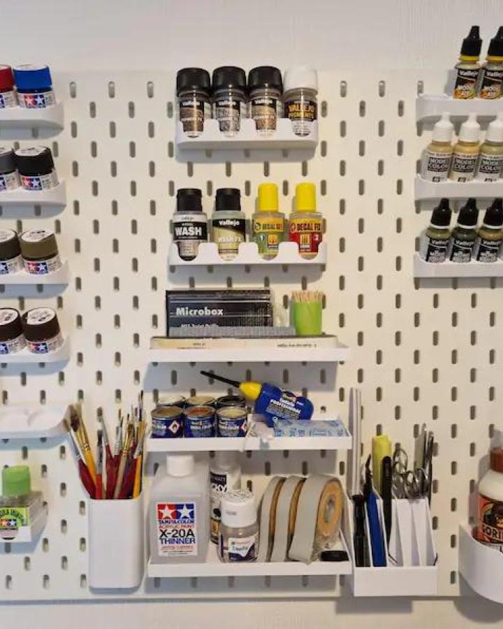 White pegboard with multi-depth shelves holding paints, brushes, and craft tools from 3DShrimping, organized for ikea craft room storage hacks.