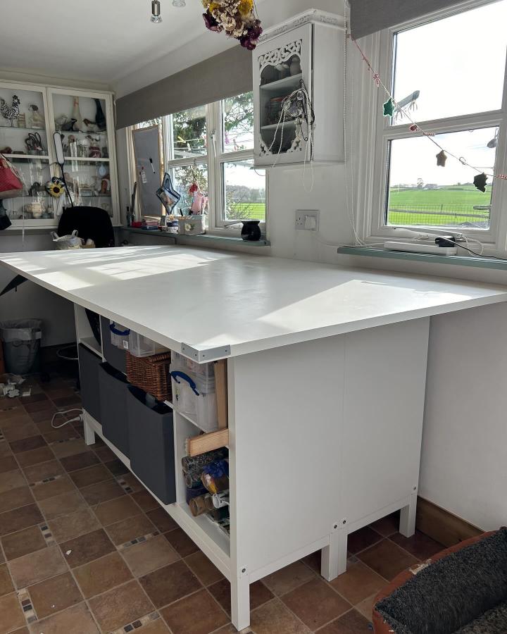 White minimalist craft table with ikea kallax craft table hacks from @sewkindco featuring open cubby storage and a smooth work surface by windows.