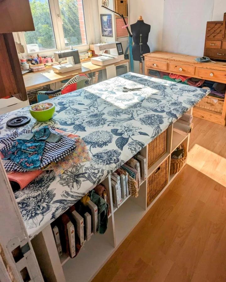 Blue and white floral fabric covered ikea kallax craft table hacks with wicker baskets and sewing supplies in bright craft room