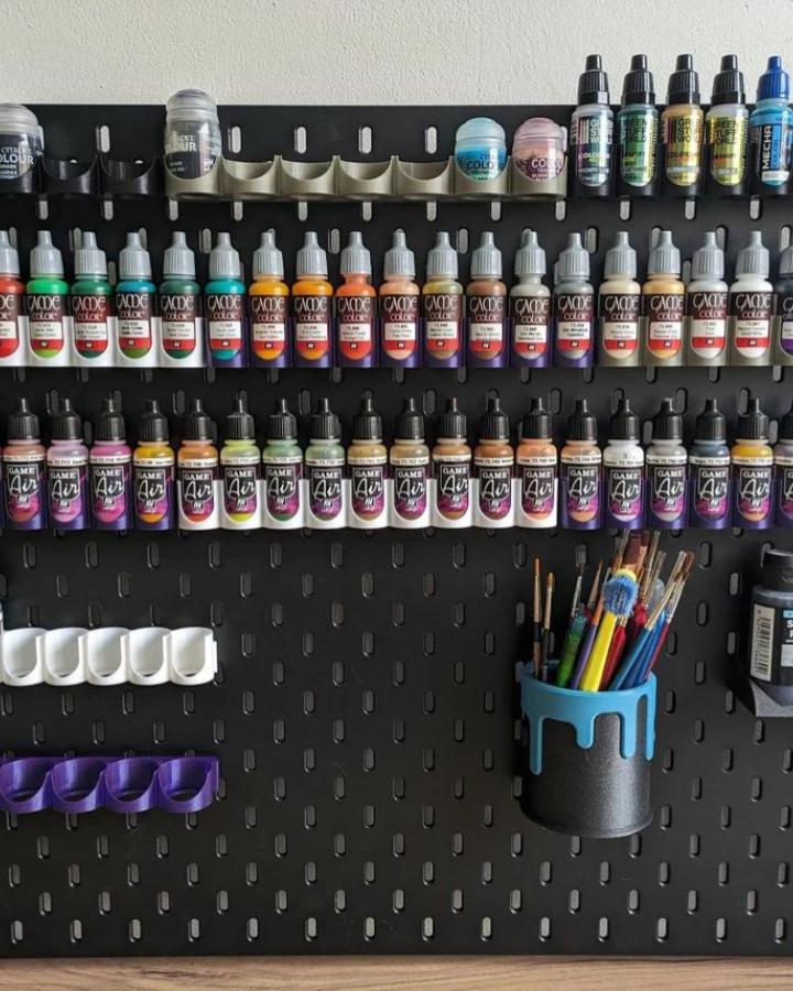 Black Ikea Skadis pegboard craft room hacks with colorful paint bottles and brush holders from Integrity3Designs showing organized art supplies.