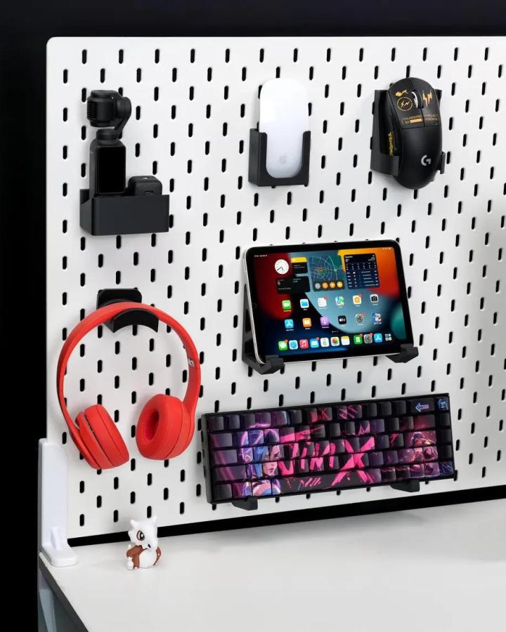 white Ikea Skadis pegboard craft room hacks from MakersFind holding headphones mouse and tablet with black holders on black wall