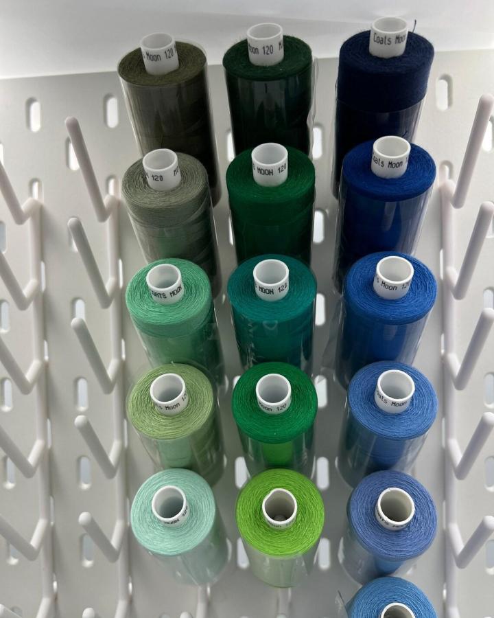 White Ikea Skadis pegboard holding colorful thread spools in green and blue hues for ikea skadis pegboard craft room hacks from DetailArtFactory.