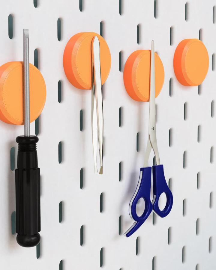 Bright orange round peg holders on white Ikea Skadis pegboard craft room hacks holding scissors and tools from Funki3d.