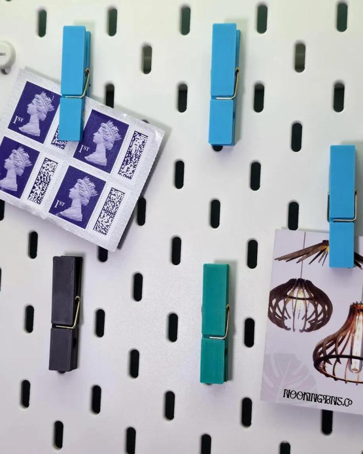 Bright colorful clothespins on white Ikea Skadis pegboard craft room hacks by NookingtonsCo holding stamps and photos.