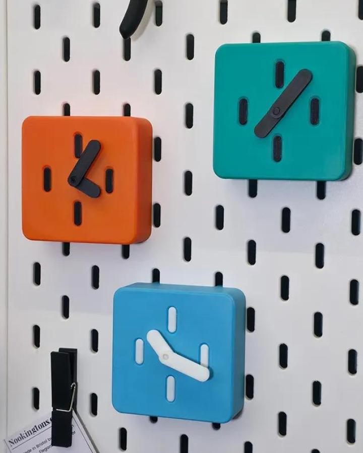 Bright colorful mini clocks on white ikea skadis pegboard craft room hacks from NookingtonsCo arranged neatly with contrasting clock hands